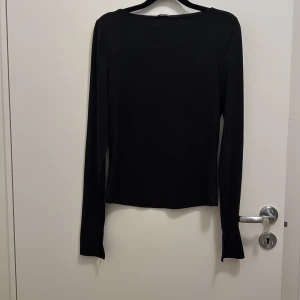 Svart långärmad topp från Bik Bok - Svart långärmad topp från Bik Bok i mjukt och stretchigt material. Toppen har en enkel, rund halsringning och cool detalj med slits vid ärmsluten. Passformen är normal och tyget känns skönt mot huden, perfekt för att styla med dina favoritjeans. Säljer likadan i mörk grått