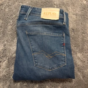 Replay Anbass Slim Fit Jeans Blå - Snygga blå jeans från Replay i modellen Anbass Slim Fit. Klassisk femficksdesign med ljus tvätt och diskreta slitningar. Jeansen har guldfärgade sömmar, logotyp på bakfickan och detaljerad etikett i midjan. Perfekta för dig som gillar en smalare passform.