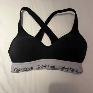 Svart linnetopp från Calvin Klein - Svart BH/topp från Calvin Klein med grå resår och logga runt om. Snygg sportig design med korsade axelband i ryggen. 