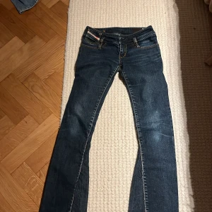 Mörkblå Diesel jeans med raka ben - Snygga mörkblå jeans från Diesel med klassiska orange sömmar och femficksdesign. Jeansen har raka ben och låg midja, samt tydliga Diesel Industry-detaljer på myntfickan. Tillverkade i slitstarkt denimtyg som ger en cool look. står ej storlek men blev precis för små för mig som är 165cm och då blev de för små i midjan som är 35 cm