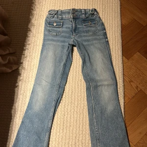 Bootcut jeans från H&M ljusblå - Ljusblå bootcut jeans från H&M med låg midja och justerbar midja. Klassisk femficksmodell med två fickor framtill med lock och knappar. Jeansen har en snygg tvätt och är tillverkade i bomullsmaterial.