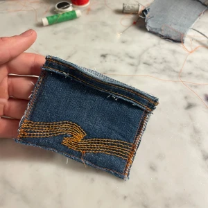 Handgjord nudie plånbok - Unik plånbok sydd av återvunnen blå denim med klassiska orangea sömmar. Perfekt för kort och smågrejer, med coolt jeansmönster och råa kanter som ger en chill vibe. Liten och smidig att ha med sig överallt. 