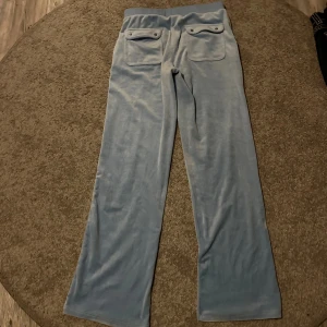 Ljusblåa juicy couture i velour - Säljer ett par ljusblå mjukisbyxor i mjuk velour med raka ben och två stora fickor bak. Byxorna har resår i midjan och en avslappnad passform, perfekta för en chill och bekväm stil.