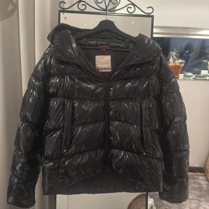Svart glansig puffig vinterjacka - Säljer denna svarta, glansiga pufferjacka från Napapijri som är perfekt om du letar efter en varm och snygg jacka till vintern 🥰 Anledningen till varför jag inte säljer den så dyrt som många andra jackor är för att den har små slit på glansiga delarna, mest vid ärmarna som man kan se på sista bilden, som dock inte är något som syns tydligt. Men annars är det varmaste jackan jag nånsin ägt! ❄️Skriv om du har frågor!