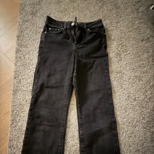 Svarta jeans från Gina Tricot - Svarta jeans från Gina Tricot med klassisk femficksdesign och dragkedja. Modellen har raka ben och rå kant nedtill. Jeansen är tillverkade i jeansmaterial och har normal passform med midwaist. Perfekt för dig som gillar stilrena och coola byxor.