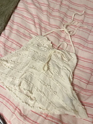 Vit spetsig linnetopp med knyt - Söt vit linnetopp med volangdetaljer och spets, samt knytband i nacken. Perfekt för varma dagar och har en romantisk vibe med sina fina strukturer och spetskanter.