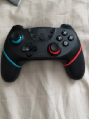 Svart trådlös spelkontroll med färgdetaljer - Snygg svart trådlös handkontroll med blå och röda detaljer runt spakarna. Kontrollen har klassisk layout med styrkors, två analoga spakar, samt A, B, X och Y-knappar. Ergonomisk form och tillverkad i plast, passar perfekt för gaming.