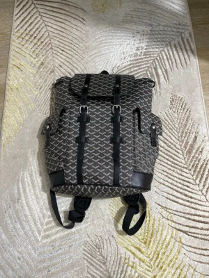 Mönstrad ryggsäck - Snygg ryggsäck i brunt och svart med det klassiska . Väskan har svarta läderdetaljer, två sidofickor med lock och spännen samt justerbara axelband. Perfekt för dig som vill ha en unik och exklusiv accessoar.