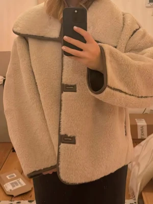 Beige oversized teddyjacka ARKET pile jacka - Säljer en trendig beige teddyjacka från ARKET med stora slag och markerade bruna detaljer längs kanterna. Jackan har oversized passform och stängs med knappar framtill. Perfekt för dig som vill ha en mysig och trendig look. Använd några få gånger. Endast köp via appen!