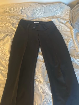 Svarta kostymbyxor med pressveck - Snygga svarta kostymbyxor med raka ben och pressveck framtill. Byxorna har hög midja, bälteshällor och stängs med två knappar och dragkedja. Perfekta till en stilren och clean look.