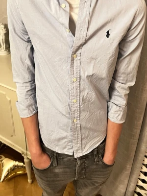 Ralph Lauren ljusblå skjorta - Ljusblå långärmad skjorta från Ralph Lauren i barnstorlek 14, motsvarande ungefär XS/XXS. Ärmarna är något korta, så den passar bäst med uppkavlade ärmar. I övrigt är skjortan i fint skick utan defekter. Kontakta vid frågor! 🤗