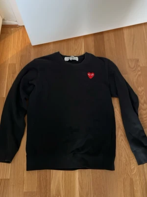  Comme des Garçons Play - Svart stickad tröja från Comme des Garçons Play med det ikoniska röda hjärtat med ögon broderat på bröstet. Tröjan har rund halsringning och långa ärmar. Enkel och stilren design som passar till mycket.