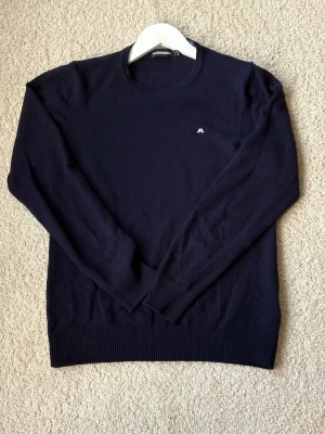  stickad tröja  J Lindeberg - Snygg mörkblå stickad tröja från J.Lindeberg med rund hals och diskret logga på bröstet. Tröjan har långa ärmar och ribbade muddar vid ärmslut och nederkant. Perfekt för dig som gillar stilrena och klassiska plagg.  . Vid frågor är det bara att skriva💫