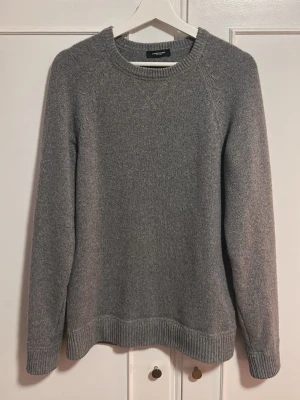 Grå stickad tröja från Lawrence Grey - Klassisk grå stickad tröja från Lawrence Grey med rund halsringning och ribbade muddar vid ärmslut och nederkant. Tröjan har en enkel och stilren design, perfekt för lager på lager och passar till det mesta. Matrialet är i kashmir tillbringat en bekvämlighet och lyxig känsla.