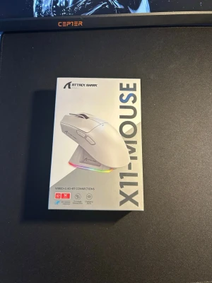 Attack Shark X11 gamingmus vit - Säljer en vit Attack Shark X11 gamingmus med RGB-belysning. Musen har trådlös och trådad anslutning, flera sidoknappar och laddningsbar funktion. Perfekt för gaming och har en modern, stilren design i plast.