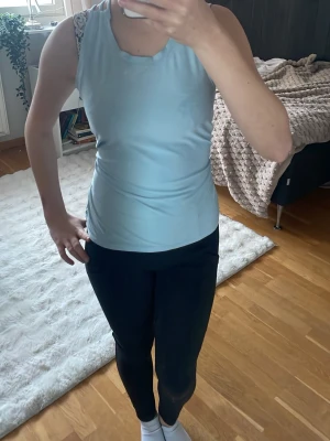 Ljusblå sport linne med korsade band - Snygg ljusblå sport linne med smala axelband som korsas i ryggen. Toppen är figurnära och tillverkad i ett mjukt, stretchigt material som känns skönt mot huden. Perfekt för en avslappnad och sportig look.