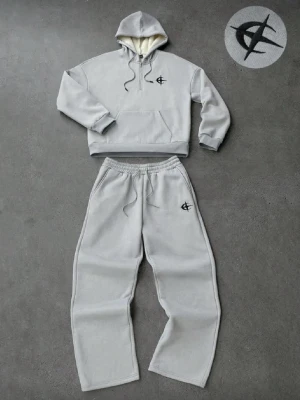 Grått loungewear-set med huva - Mysigt grått loungewear-set med hoodie och matchande byxor. Hoodien har dragsko, magficka och mjukt foder, samt svart broderad logga på bröstet. Byxorna har resår i midjan, dragsko och samma logga på benet. Perfekt för chill dagar hemma.