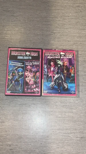 Monster High Dvd - Två DVD-filmer från Monster High: 'Dubbeläventyr' och 'Monstren Regerar'. Omslagen är färgglada med karaktärer från Monster High-serien. Perfekt för dig som gillar animerade äventyr och coola monster. Båda filmerna är på svenska och har snygga rosa och svarta fodral. Förekommer repor på skivan och ena fodralet lite förstört men inget som påverkar!.