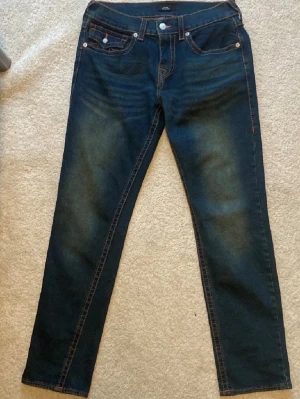 Mörkblå jeans från True Religion - Snygga mörkblå jeans från True Religion med klassiska kontrastsömmar och ikoniska bakfickor med lock och knapp. Jeansen har en rak passform. Prisej ej fast 👍