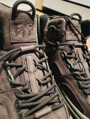 Grå höga sneakers från Eytys - Säljer ett par bruna höga sneakers från Eytys med robust design och tjock sula. Skorna har svarta snören, detaljerade sömmar och är tillverkade i läderliknande material. Perfekta för dig som gillar streetwear och vill sticka ut med en unik look.