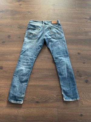 Blå slitna jeans från Jack and Jones - Säljer ett par blå jeans från Diesel med snyggt slitna detaljer och raka ben. Jeansen har klassiska fem fickor, synliga sömmar. Perfekta för en avslappnad och trendig look. Ett litet hål vid bakfickan.