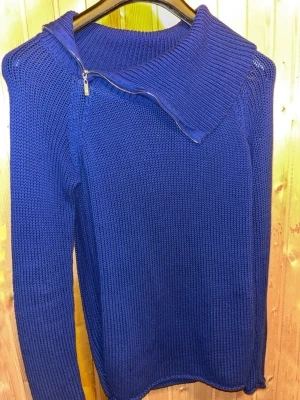 Blå stickad tröja från Guess - Snygg blå stickad tröja från Guess med stor krage och dragkedja vid halsen. Tröjan har lång ärm och är gjord i ett tjockare stickat material som känns både trendigt och bekvämt. Perfekt för dig som vill ha en unik detalj i garderoben.