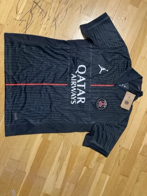 Svart PSG matchtröja - Snygg svart PSG matchtröja från Jordan med Dri-FIT material. Tröjan har vita och röda detaljer, PSG-logga på bröstet och Qatar Airways tryckt framtill. Perfekt för fotboll eller streetwear. Tillverkad i Thailand och har en klassisk passform. Priset kan diskuteras 🤝