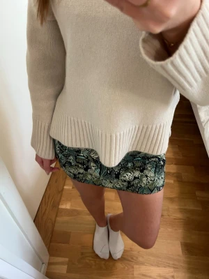 Grön blommig kortkjol - Snygg kortkjol med blommigt mönster i gröna och svarta toner. Kjolen har en figurnära passform och är perfekt för dig som vill sticka ut med en cool och trendig look. Passar till både stickad tröja och t-shirt.