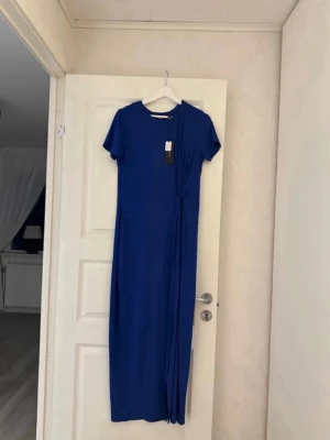 Blå klänning från Vero Moda  - Snygg blå långklänning från Vero Moda med rund halsringning och korta ärmar. Sitter tajt mot kroppen Klänningen har en slits. 