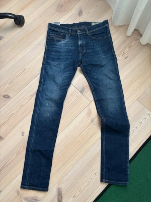 Mörkblå jeans från Diesel - Snygga mörkblå jeans från Diesel med klassisk femficksdesign och diskreta slitningar. Jeansen har smal passform och detaljerade sömmar samt en liten logotyp på myntfickan. Perfekta för en trendig och avslappnad look. I nyskick.