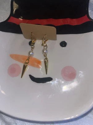 Guldörhängen med pärlor och spikes - Säljer ett par trendiga örhängen i guldfärgad metall med vita pärlor och coola spetsiga spikes. Perfekta för dig som vill ha en edgy men ändå elegant look. Örhängena har krokfäste och hänger snyggt från örat.