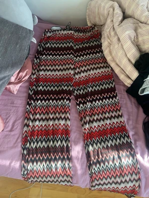 Mjukisbyxor med zigzag-mönster - Färgglada mjukisbyxor med zigzag-mönster i rött, svart, vitt och beige. Byxorna har en lös passform och resår i midjan för extra komfort. Perfekta för en chill och avslappnad stil.