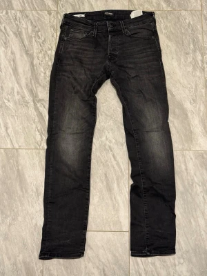 Svarta slim fit jeans från Jack & Jones - Snygga svarta slim fit jeans från Jack & Jones med klassisk femficksmodell och diskreta slitningar. Jeansen har normal midja, dragkedjegylf och är tillverkade i stretchigt denim för extra komfort. Perfekta till en avslappnad streetstyle-look.
