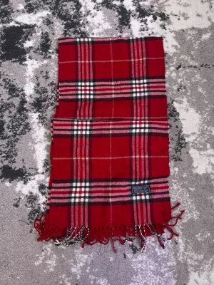 Röd rutig halsduk från Burberry - Klassisk röd halsduk från Burberry i 100% lammull med ikoniskt rutmönster i svart, vitt och beige. Halsduken har fransar i ändarna och en vävd Burberry-etikett. Perfekt accessoar för att lyfta din outfit med en tidlös touch.