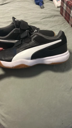 Svarta Puma Tenaz sneakers med kardborre - Snygga svarta Puma Tenaz sneakers med vit sula och vit logga på sidan i storlek 35. Skorna har kardborreband för enkel påtagning och en gummisula med bra grepp. Ovandelen är i syntetmaterial och mesh för bra ventilation. Perfekta för dig som gillar sportig stil.