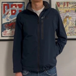 Helly Hansen Jacka - Säljer denna Mörkblåa höstjacka från Helly Hansen. Jackan är fodrad så håller värmen ganska bra. Bra skick, inga fläckar, revor eller hål. Size S passar M. Modellen på bilden är 182cm lång ish. Skriv vid funderingar!