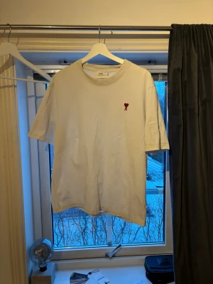 Ami Paris T-shirt - En vit T-shirt från märket Ami Paris i storlek L. Tröjan är köpt på nk i Stockholm sommaren 2025 och har använts sparsamt sedan dess.   Priset går att diskuteras vid snabb affär! Hör av er vid funderingar!