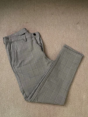 Grå rutiga kostymbyxor från Zara - Säljer ett par stilrena grå kostymbyxor från Zara med diskret rutmönster. Byxorna har normal passform, bälteshällor och knappstängning. Perfekta för dig som vill ha en clean och modern look.