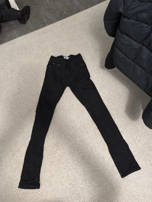 Svarta skinny jeans från 157, W28 L32 - Svarta jeans från 157 med skinny passform och klassisk femficksdesign. Byxorna har normal midja och är tillverkade i bomull med lite stretch för extra komfort. Perfekta för dig som gillar en tajt siluett och stilren look.