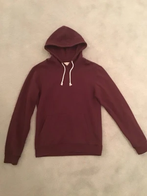 Vinröd Hoodie med vita snören - Säljer en vinröd hoodie från pier one perfekt för dig som vill ha en enkel, snygg och bekväm hoodie i vardagen. 