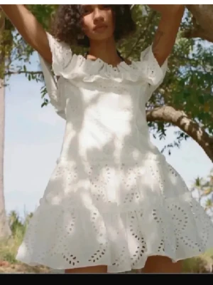 Vit volangklänning med broderi - Superfin vit kortklänning med volanger och broderade detaljer. Klänningen har offshoulder-ärmar och är gjord i ett lätt bomullstyg. Perfekt för varma dagar och har en luftig passform med romantiska broderier och söt volangkant upptill.