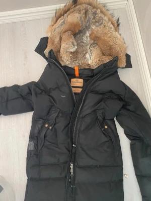 Parajumper longbear jacka  - Svart dunjacka från Parajumpers med fluffig päls i huvan och coola detaljer som orange och gul rem. Jackan har dragkedja, flera fickor med knappar och är långärmad. Perfekt för kalla dagar och har en riktigt schysst look. Helt ny och pris kan diskuteras. OBS extra knappar och dragkedja finns med.