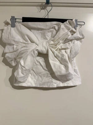 Topp med stor rosett - Vit tubtopp med rosett över bröstet. Jättesnygg och har dragkedja i sidan. 