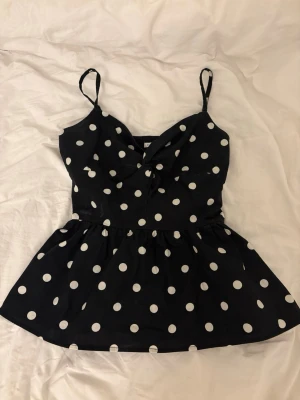 Svart prickig linnetopp med volang - Säljer en svart linnetopp med vita prickar och justerbara smala axelband. Toppen är jätte fin men säljer vidare för att den inte passade 💖💖
