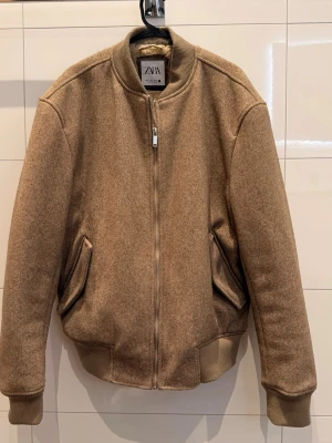 Beige teddy bomberjacka från Zara - Säljer en beige teddy bomberjacka från Zara med mjukt och fluffigt foder. Jackan har ribbade muddar, dragkedja framtill och två snedställda fickor. Perfekt för kalla dagar när du vill vara både varm och snygg.