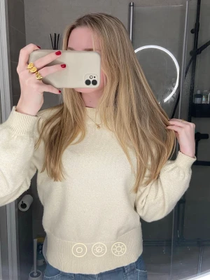 Beige stickad tröja med rund hals - Mysig beige stickad tröja med rund halsringning och breda ribbade muddar vid ärmslut och nederkant. Tröjan har en klassisk, enkel design och är lätt att matcha med olika outfits. Perfekt för lager-på-lager under kyligare dagar.