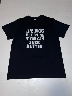 ”Life sucks but dm me if you can suck better” T-shirt - Svart T-shirt med kaxigt statement som garanterat drar blickarna till sig. Perfekt för dig med humor, attityd och självdistans. Bekväm passform och tydligt tryck – en tröja som säger det du tänker, högt och tydligt.