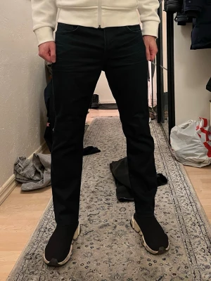 Mörk blå straight jeans/chinos från Hugo Boss - Säljer ett par mörk blå jeans/chinos från Hugo Boss med klassisk straight fit och fem fickor. Jeansen har en enkel design med mörk ton och är tillverkade i slitstarkt denim. Passar dig som gillar en clean och tidlös look.