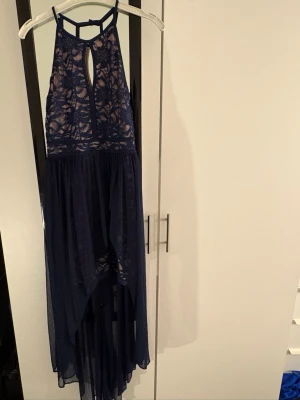 Marinblå långklänning med spets - Säljer en marinblå långklänning med spetsdetaljer och transparent mesh upptill. Klänningen har ett snyggt nyckelhålsformat urtag fram och bak, samt tunna axelband och ett flowigt, asymmetriskt kjolparti. OBS! Finns ingen tydlig storlek men passar från XS-S. 