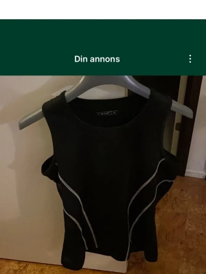 Svart träningstopp från SOC - Svart ärmlös träningstopp från SOC i storlek 42. Toppen har rund hals och snygga vita linjer längs sidorna som ger en sportig look. Perfekt för gymmet eller löprundan. Materialet är troligtvis polyester för bra komfort och rörelsefrihet.